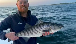 Hunter Lamere smiles and holds a large fish while standing on a boat in open water